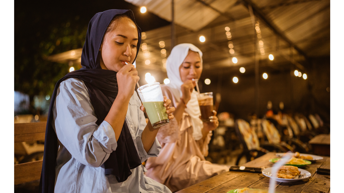 Two women wearing hijabs enjoy drinks at an outdoor cafe at night.