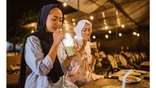 Two women wearing hijabs enjoy drinks at an outdoor cafe at night.