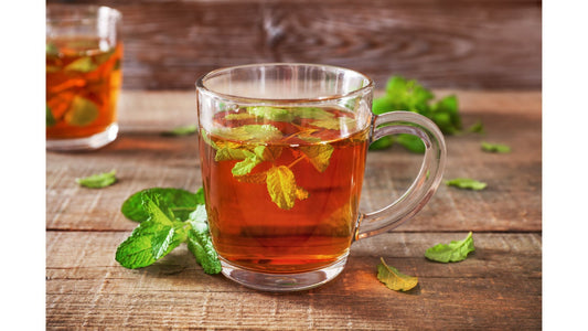A clear glass mug filled with tulsi tea and fresh green tulsi leaves, sitting on a rustic wooden surface.